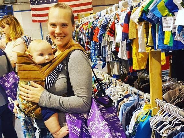 Mom carrying baby in a front carrier is standing next to clothing racks